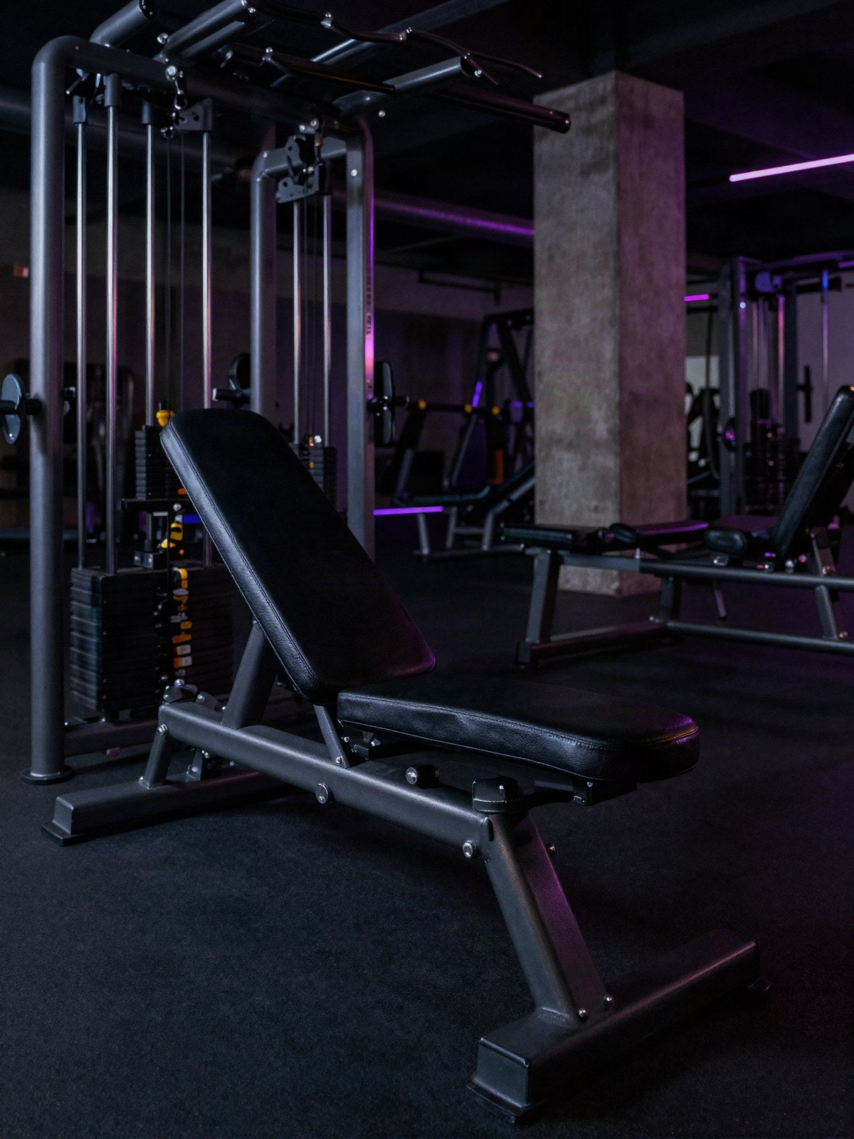 Banco de ejercicio y maquina de poleas en un gimnasio oscuro con luz violeta