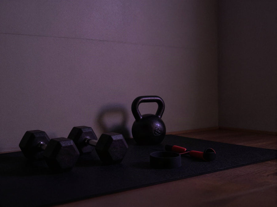 Rincon de entrenamiento en casa con mancuernas y una pesa rusa, luz violeta tenue