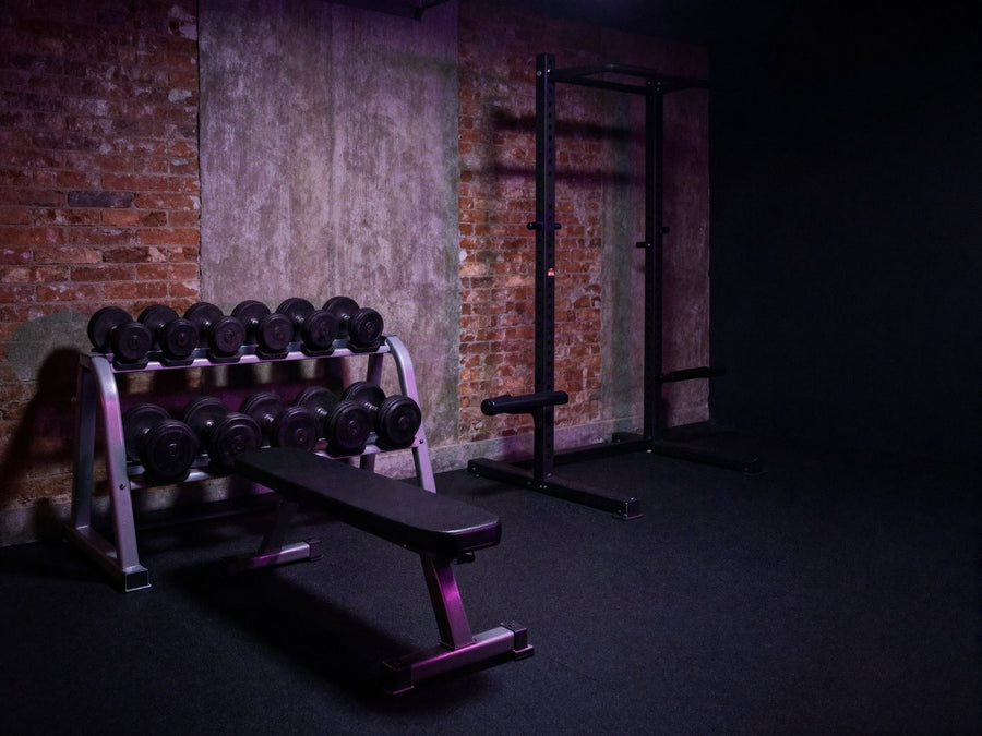 Estudio de entrenamiento pequeno con un rack de mancuernas y un banco, luz violeta